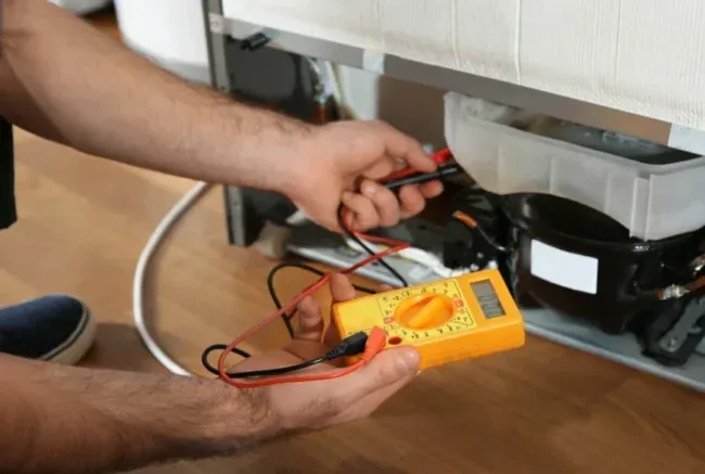 Multímetro medindo o compressor na parte de trás de um refrigerador