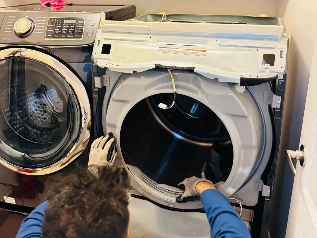 Técnico de luvas atendendo uma secadora aberta em uma lavanderia residencial